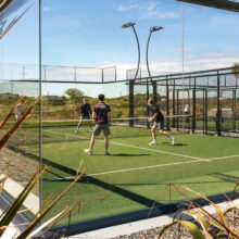 Guests enjoying a sunny day playing on a modern glass-enclosed padel court at our resort; perfect for active holidays.