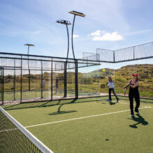Guests enjoy a sunny game of padel tennis on a well-maintained court with scenic mountain views.