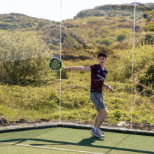 Guest playing padel on scenic outdoor court, surrounded by lush greenery and hills at luxury hotel resort.