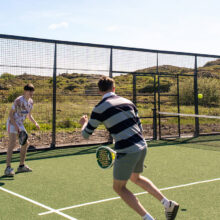 Guests enjoying a sunny game of padel tennis on the hotel's outdoor court surrounded by lush greenery.