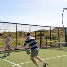 Two guests enjoy a sunny day playing paddle tennis on a modern court with scenic countryside views at a luxury hotel.