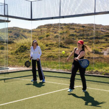 Guests enjoy a scenic padel match on a lush, outdoor court with hill views at a luxury hotel.