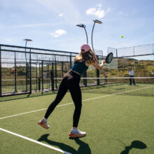 Guests enjoying outdoor tennis court under clear sky, surrounded by lush greenery at luxury hotel.