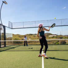 Guests playing tennis on sunlit outdoor court with scenic views at resort, perfect for active holidaymakers.