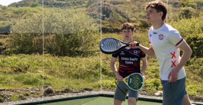 Guests enjoy a lively padel game on scenic outdoor court with lush hills in background.