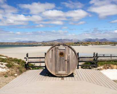 Scenic beach view with unique round sauna, sandy shoreline, and distant mountains; perfect for relaxing holidays.