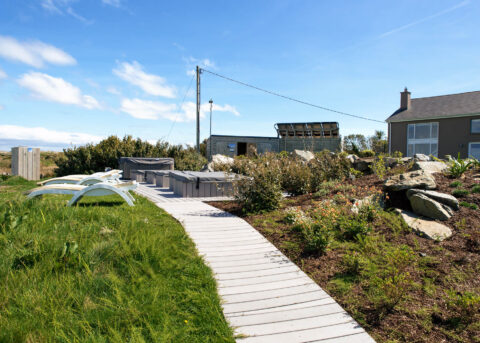 Serene hotel garden path with sun loungers, lush greenery, and cosy seating area under a bright blue sky.